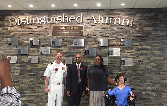 (from left to right) Nicholas Tilbrook, Samir Soneji, Maudlyne Ihejirika and Amy Liss pose in front of the Distinguished Alumni wall. 