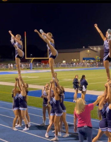 The cheerleading hits their heel stretches, while cheering for the boys football game.