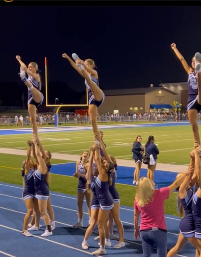 The cheerleading hits their heel stretches, while cheering for the boys' football game.