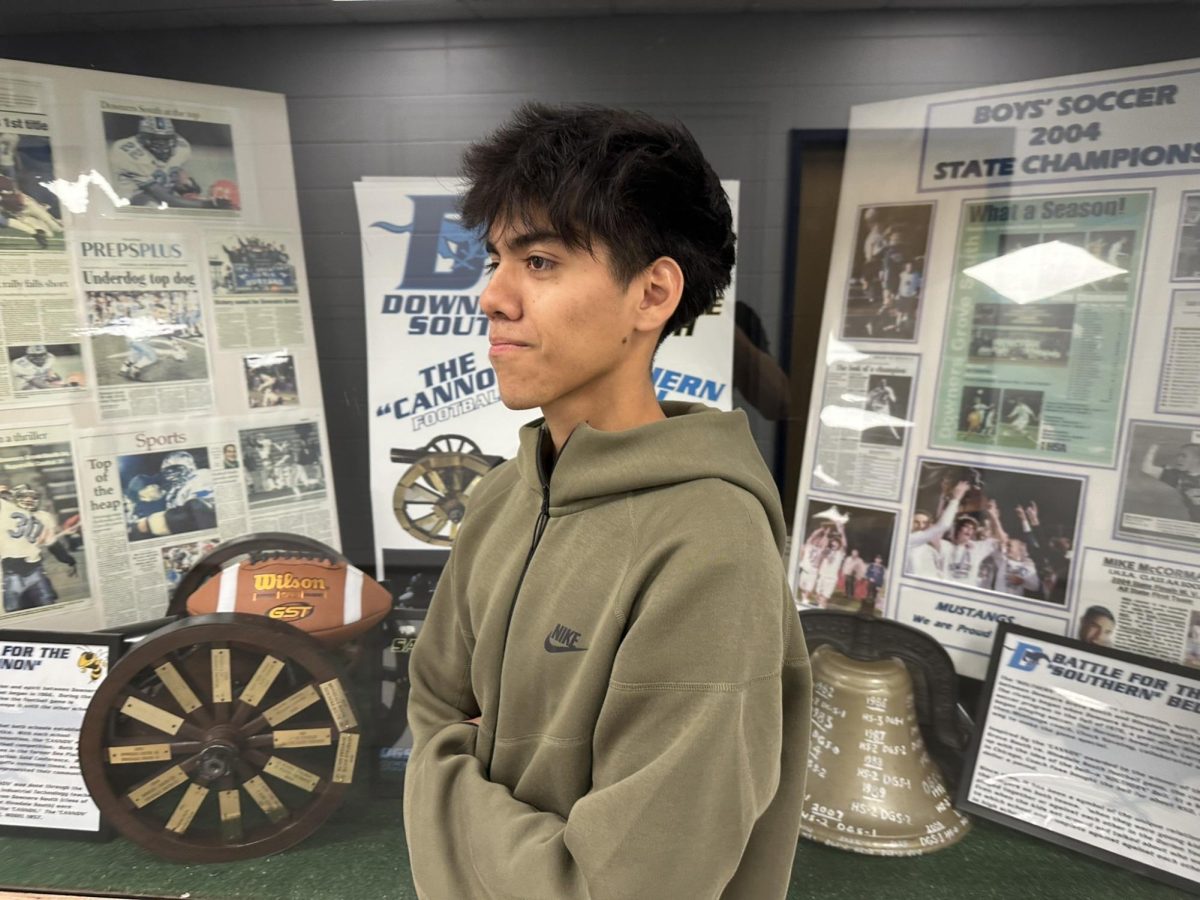 Senior varsity player Cristan Aguilar stands near the DGS display of soccer trophies.