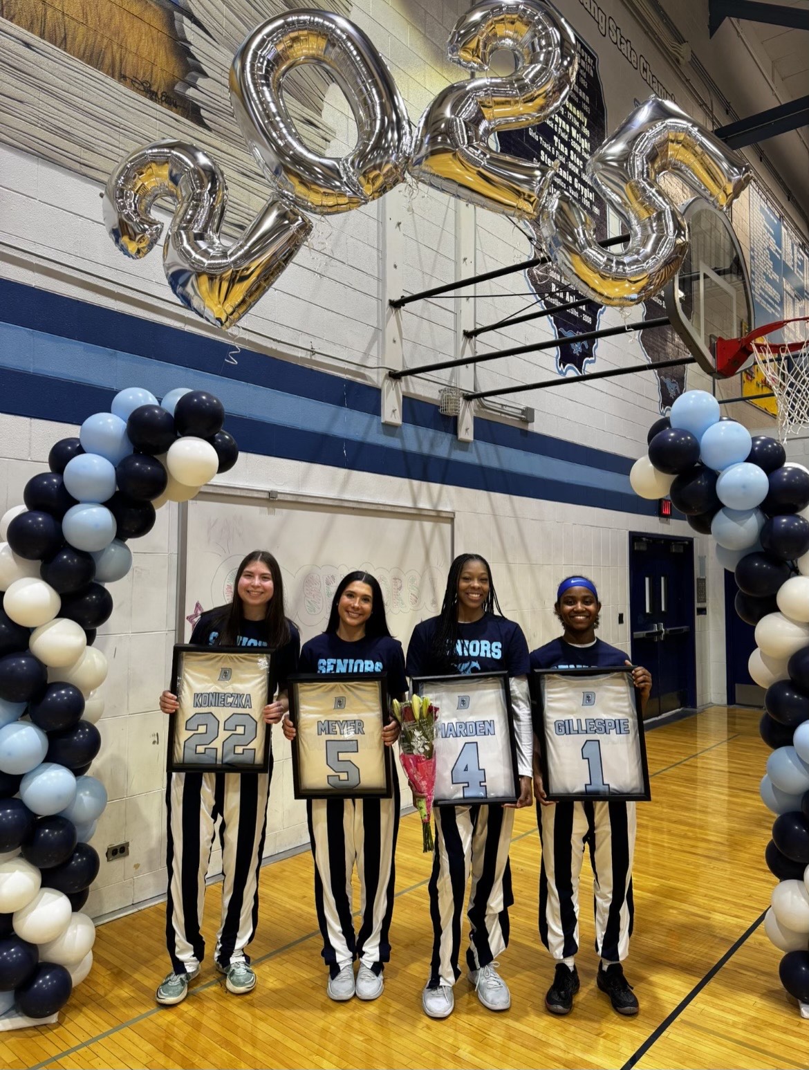 Varsity girls basketball players pose for a senior night photo with framed jerseys.