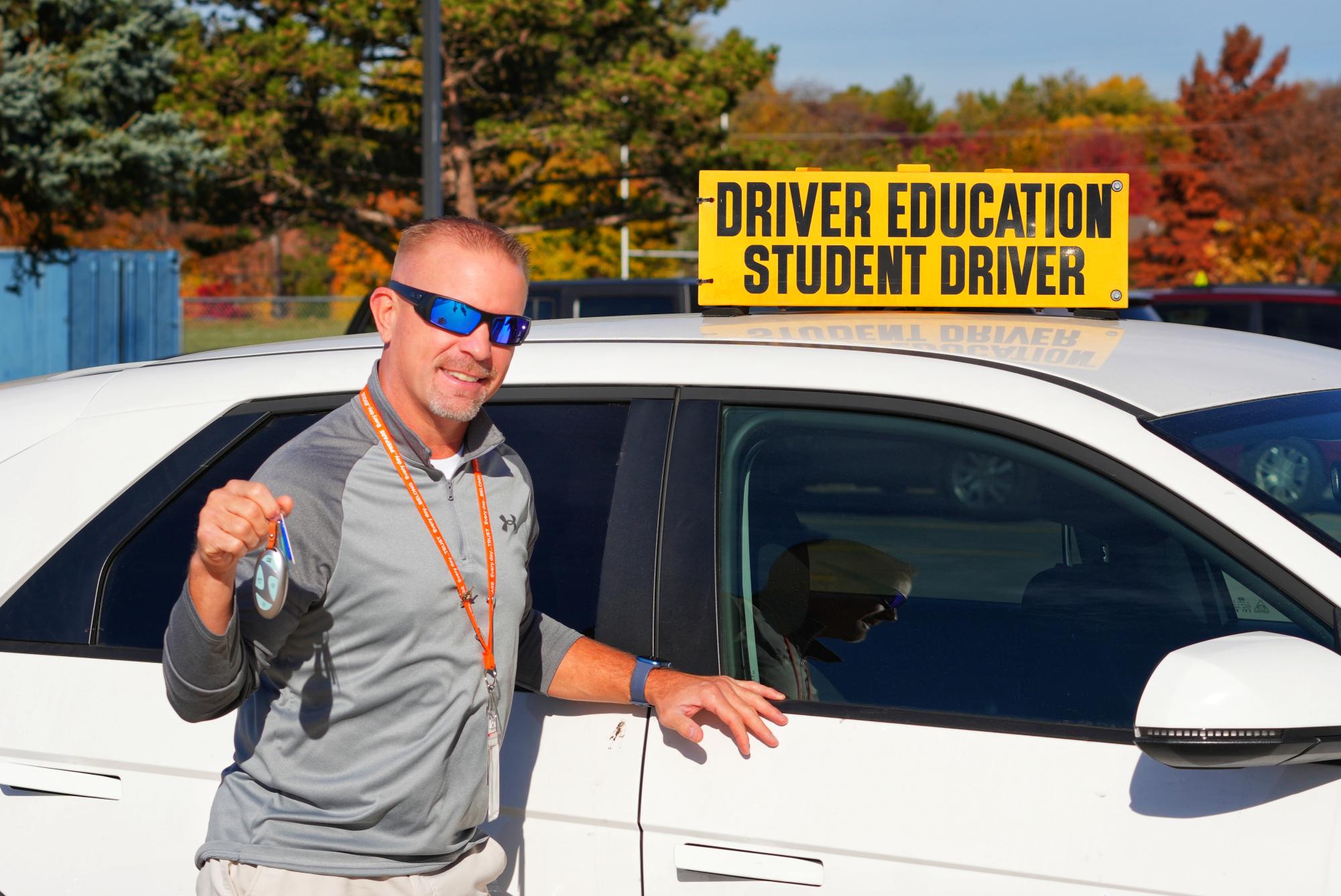 Driver's Education teacher Timothy Cappelen stands in front of the car he uses to teach students to drive. As students learn to navigate the road from empty parking lots to busy streets, they begin to build upon their knowledge and skills as a result of their driver's education teacher's guidance. 